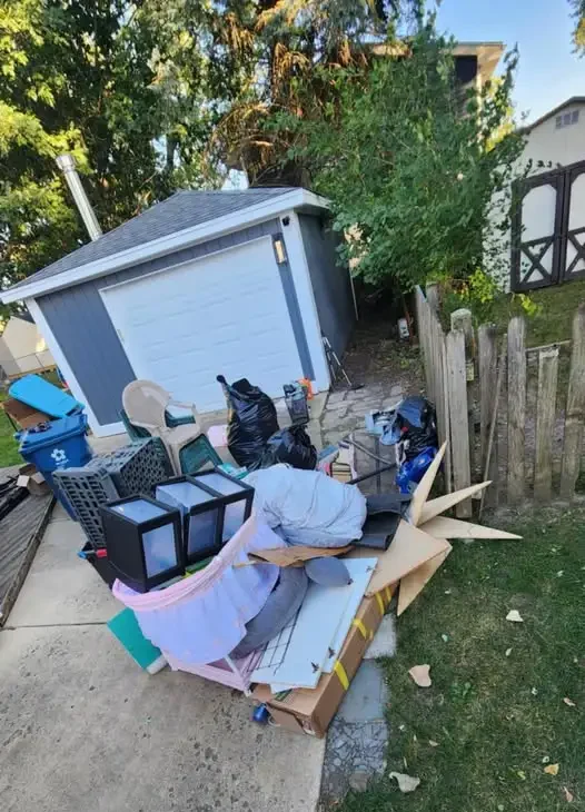 Piled-up household junk including boxes, furniture, and bags placed outside a garage for junk removal in Asheville.