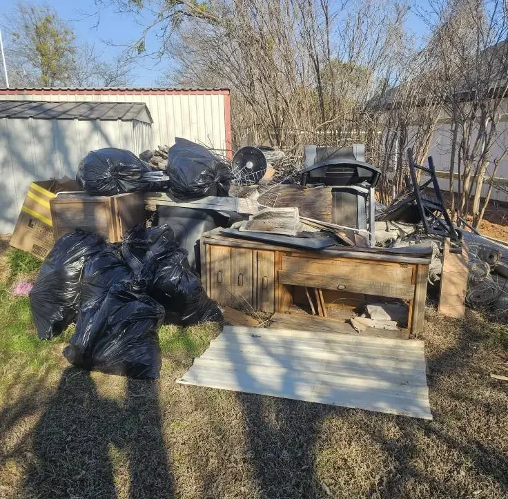 Piled-up junk and trash bags in a backyard before junk removal