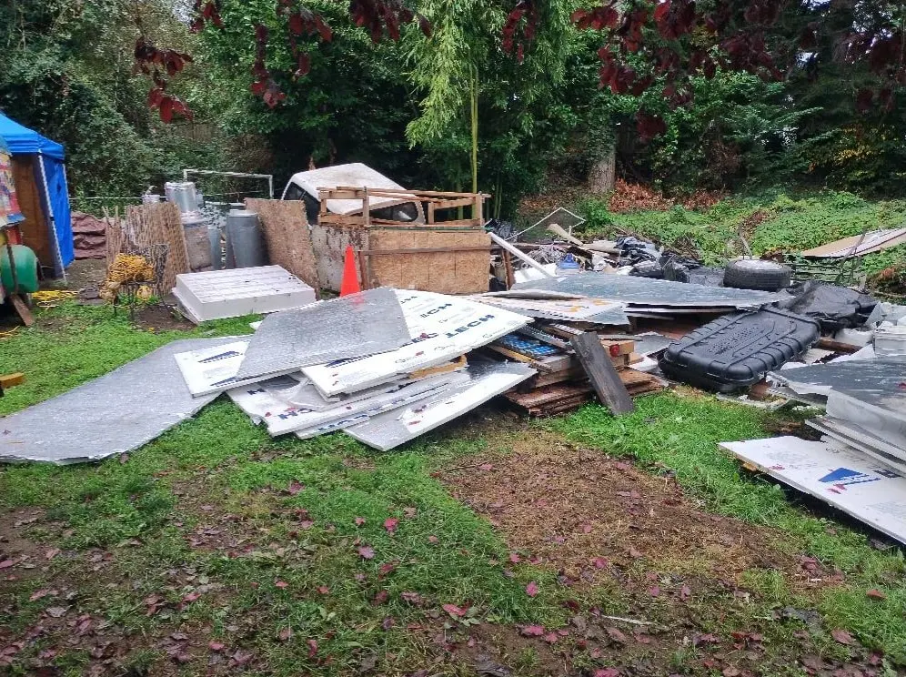 Large pile of metal panels, insulation boards, and construction debris scattered in a backyard awaiting junk pickup in Asheville.