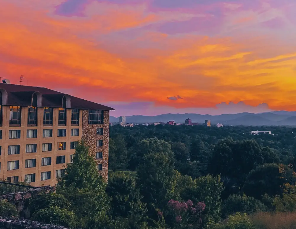 Colorful sunset over Montford, Asheville with scenic mountains and buildings surrounded by trees.