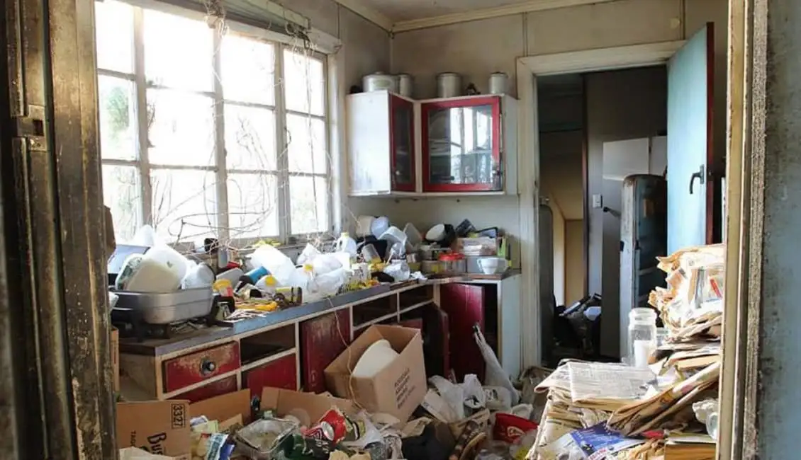 Cluttered kitchen filled with trash, old dishes, and paper waste before junk removal