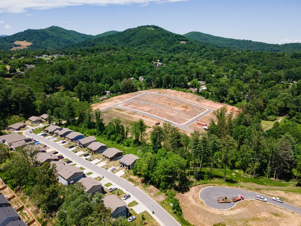 Aerial view of a residential neighborhood and new development in West Asheville, North Carolina, surrounded by mountains and trees.