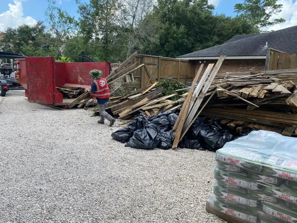 Worker cleaning up storm debris and wooden waste near a red dumpster