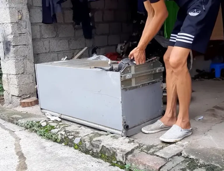 Person moving an old broken refrigerator outside a residential property in Asheville NC for appliance removal and recycling