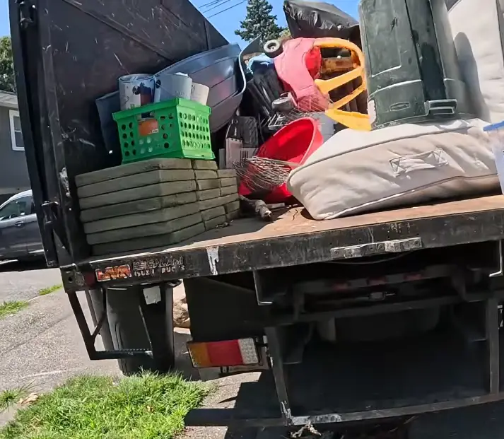 Flatbed junk removal truck loaded with household items including stepping stones, bins, and outdoor furniture after a residential cleanout in Asheville NC